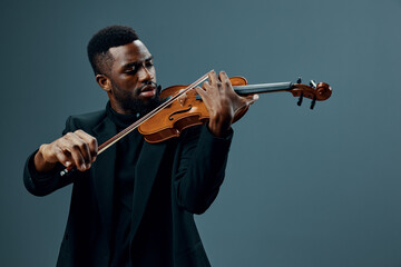 African American man in black suit playing violin, creating soulful music on gray background