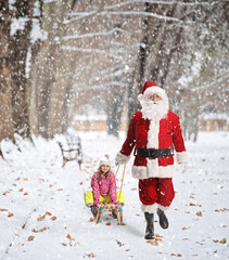 Santa claus pulling a child on a wooden sled in a park