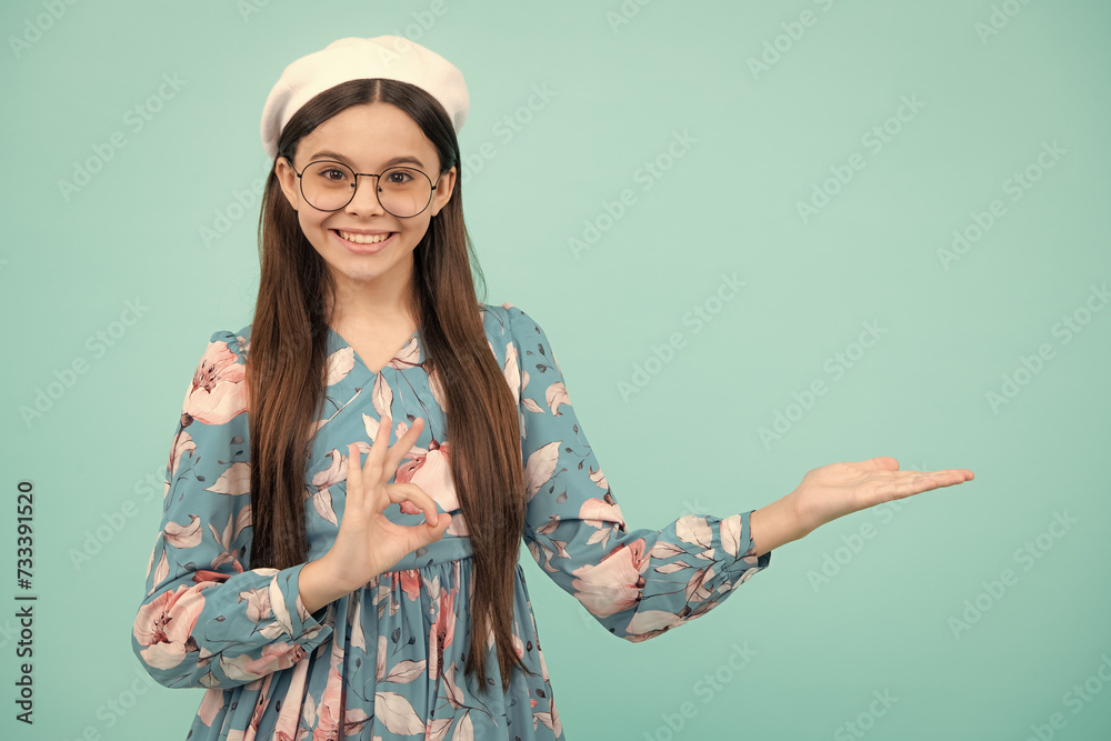 Wall mural Happy teenager, positive and smiling emotions. Close up portrait of teenager child girl showing at copy space, pointing to ads advertising, isolated over white background.