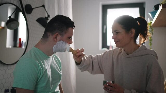Mother applying shaving foam on son's face. Young man with down syndrome learning how to shave.