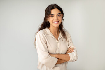 Smiling young woman standing confidently with arms crossed over light background