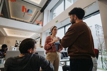 Fototapeta premium Two professionals casually interacting with each other in a bright, contemporary office space, with co-workers in the background.