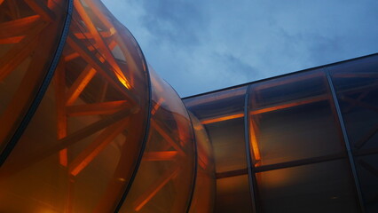 Structure de bâtiment de voile ou high-tech, avec éclairage intérieur de lumière, en plein milieu d'un grand parc parisien, ciel sombre et nuageux, bleu foncé, début de soirée, avec végétation morte