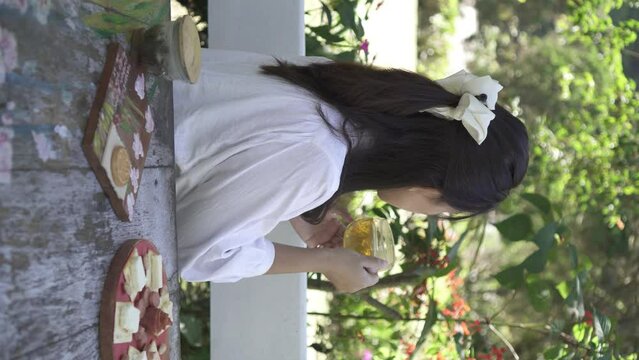 A beautiful asian woman in white is sipping a glass of hot tea in the morning with bokeh garden backgrounds. Herbal drinks, Alternative medicine, Healthy food, Relaxation, Leisure activity concept