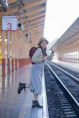 Rear view of a young woman with backpack standing on a train station, travel concept, Portrait of Asian woman tourist waiting for the train at railway station