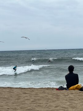 A surfer in the sea and a man watching the surfer from the sea with seagulls flying around.