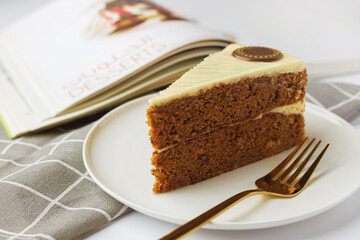 Slice of carrot cake on a white plate with a book in the background
