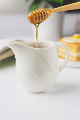 Honey dripping from a wooden honey dipper into a Small jug