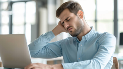 young man in business casual attire sitting at a desk, working on a laptop, and experiencing neck pain, likely due to poor posture or prolonged sitting.