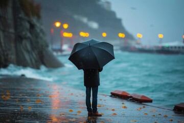 Amidst the foggy beach, a person stands with an umbrella, braving the rainy sky and wet ground with determination - obrazy, fototapety, plakaty