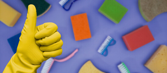 Cleaner's hand in yellow kitchen glove on blurred background of cleanliness kit. Banner or header...