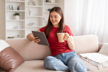 Relaxed young asian woman holding digital tablet and coffee mug