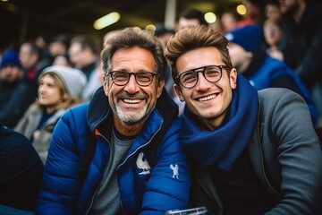 French father and son in stands supporting national sports team with enthusiastic blue-clad fans