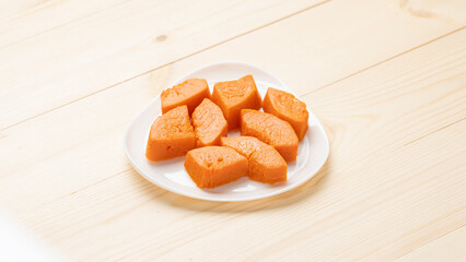 Pieces of baked pumpkin on a white plate on a wooden table, top view, close-up.