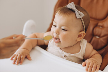 Mother feeding healthy food to her adorable little daughter sitting in high chair