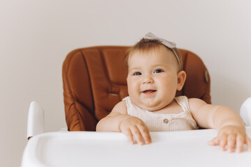 Happy little baby girl sitting in high chair in kitchen at home