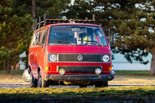 Red old classic minivan Volkswagen Transporter T3 from the 80s stands outside in a parking lot at sunset.