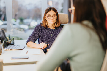 Two women colleagues in an office setting, deeply involved in a business discussion, portraying...