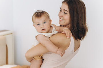 Happy mother with her beautiful little baby daughter in the bedroom on the bed