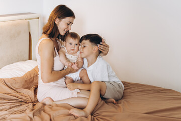 Naklejka na ściany i meble Happy young mother spending time with her children in the bedroom