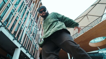 Low angle view of hipster pose in hip hop style surrounded by mall view. Portrait of sporty asian hip hop choreographer dancing break dance while looking at camera. Outdoor sport 2024. Endeavor. - obrazy, fototapety, plakaty