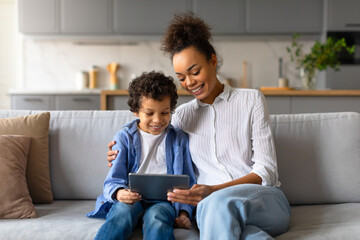 Black mother and son enjoying tablet time together on cozy sofa