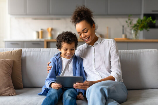 Black mother and son enjoying tablet time together on cozy sofa