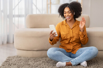 Joyful African American woman wearing a mustard shirt and blue jeans sitting cross-legged