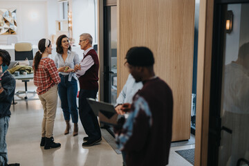 Two women and a man having a friendly conversation in a modern office environment, exemplifying teamwork and casual business discussions.