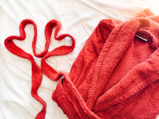 A red bath robe close up and a belt shaped like two hearts is on the white bed. Valentine’s Day...