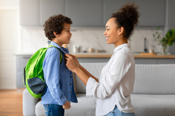 Happy black mother preparing child boy with backpack for school - obrazy, fototapety, plakaty