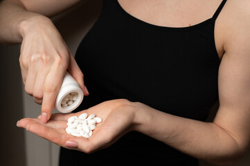 Female hands pour out handful of white pills tabs from the jar to take medication to kill pain