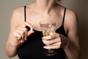 Self help medication concept: woman holds glass of water and a pill to kill the pain, prescribed supplement medication