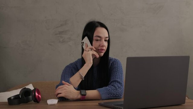 The girl is talking on the phone while sitting at the laptop in the room