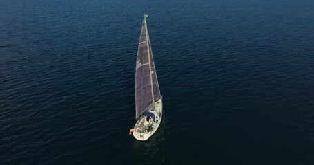 Beautiful sailboat sailing in tropical exotic bay with deep blue sea. Establishing aerial shot of the yacht in the rays of the setting sun. Silhouette of a sailing yacht in the sea shot from a drone