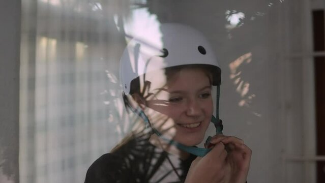 A beautiful blonde puts a white bicycle helmet on her head. The video was shot through the window.
