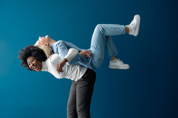 Happy young women enjoying themselves while being playful against a blue background. Interracial...