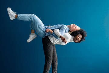 Energetic young woman carrying her best friend on her back in a studio. Two interracial best...