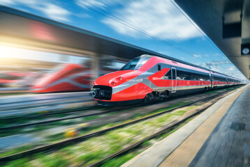 Red high speed train in motion on the railway station at sunset