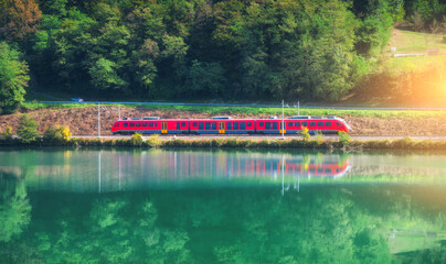 Red modern high speed train and river in mountains at sunrise