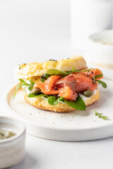 Homemade bagel sandwich with smoked salmon, cream cheese, capers and spinach for healthy breakfast on white kitchen background for breakfast