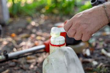 A gardener pours oil into a can of gasoline to refuel a lawnmower. Fuel preparation.