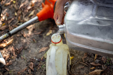 Obraz premium A gardener pours gasoline from a can into a plastic container for refilling a lawn mower.