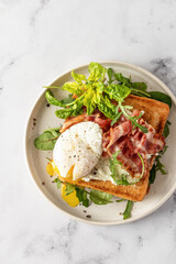 Toasts sandwich with poached egg, arugula, bacon and cream cheese on white plate marble background