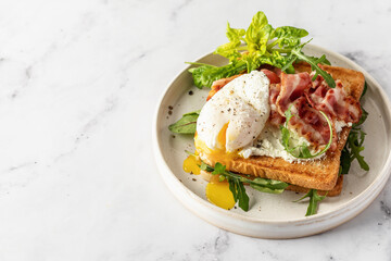 Toasts sandwich with poached egg, arugula, bacon and cream cheese on white plate marble background
