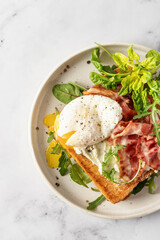Toasts sandwich with poached egg, arugula, bacon and cream cheese on white plate marble background