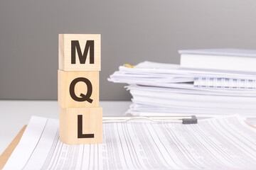 text MQL - Marketing Qualified Lead - on wooden blocks. the background is a business papers. finance concept. white background