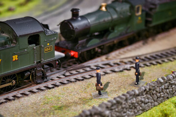 Close-up shot of miniature figures next to a model train track with detailed old-fashioned steam engine locomotives