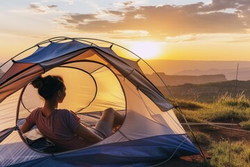 A woman sitting inside of a tent at sunset.