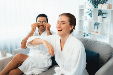 Blissful couple in bathrobe playing with cucumber and enjoying daylight ambiance spa salon resort or hotel during holiday. Pampering face spa and skincare treatment with essence relaxation. Quiescent
